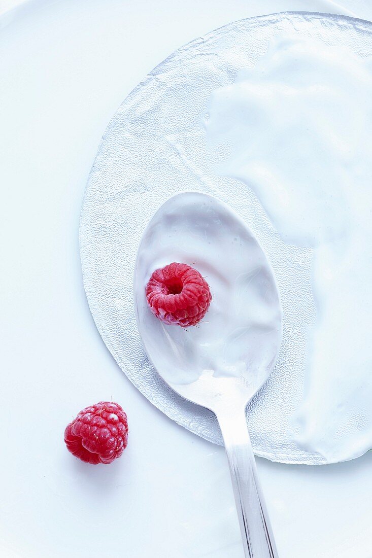 An aluminium lid and a spoon of cream cheese with raspberries