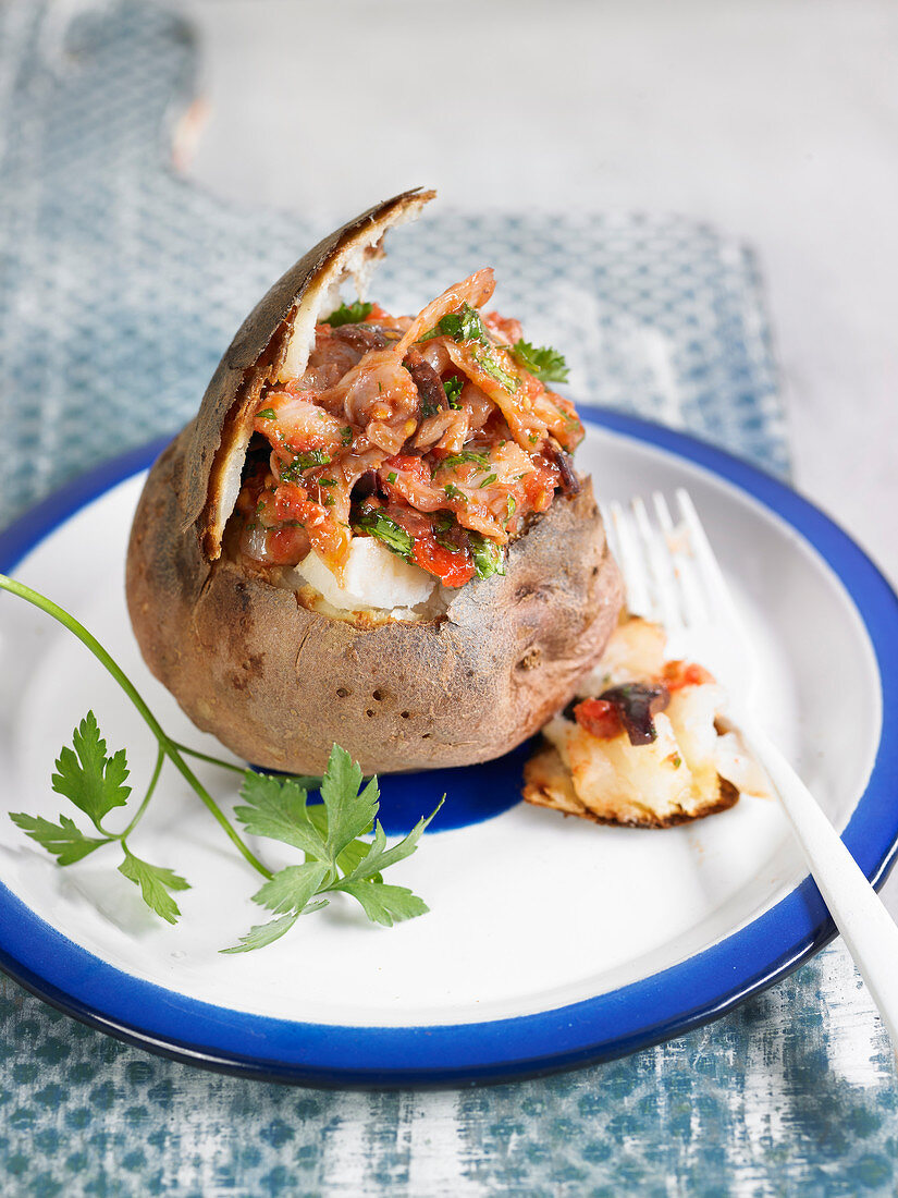 Baked potato stuffed with smoked cod, olives, tomatoes and parsley