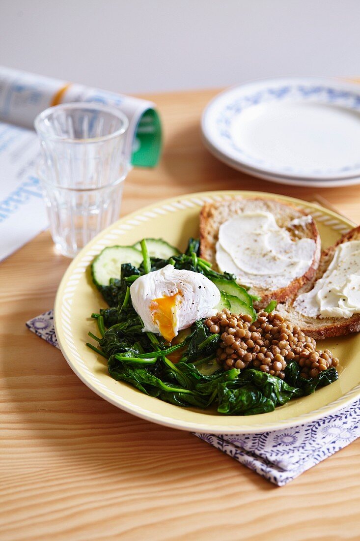 A plate of spinach, cucumber, lentils and a poached egg with toast spread with cream cheese