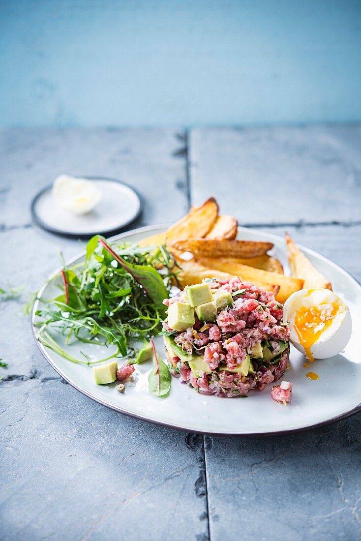 Beef tatar with avocado, a soft-boiled egg and chips