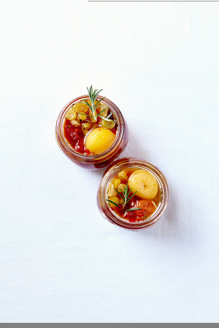 Eingemachte gelbe Pflaumen mit Tomaten, Sultaninen und Rosmarin in Einmachgläsern