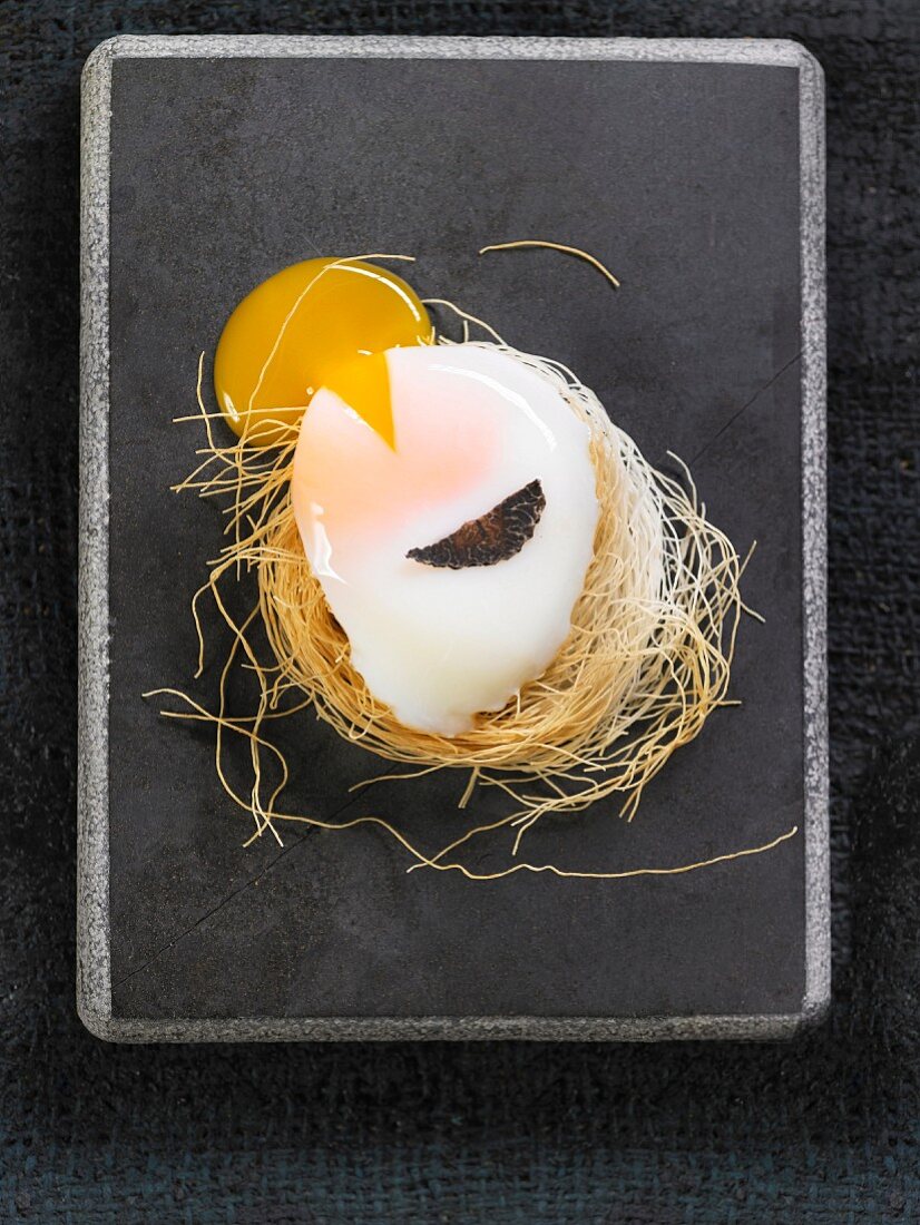A soft-boiled egg with a slice of truffle in a nest of dried pasta
