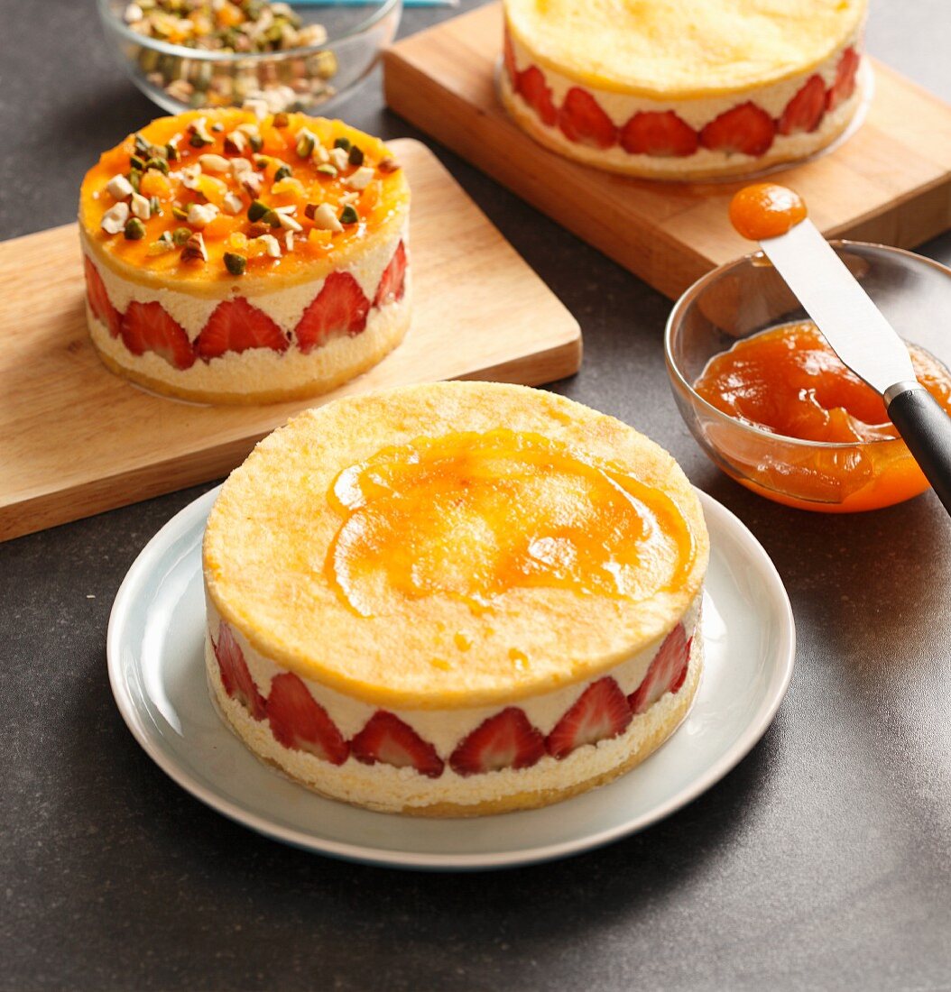 A strawberry cream cake being spread with apricot jam