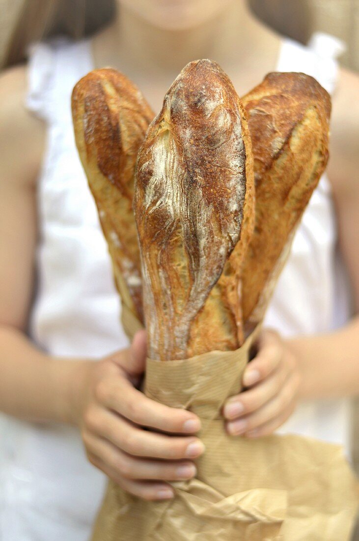 Mädchen hält eine Papiertüte mit drei Baguettes