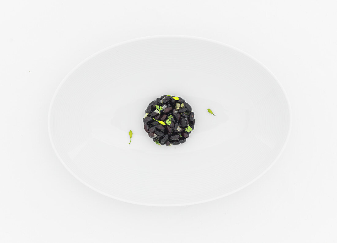 Schwarzer Bohnensalat mit Kerbel und Pfefferschoten auf weißem Teller
