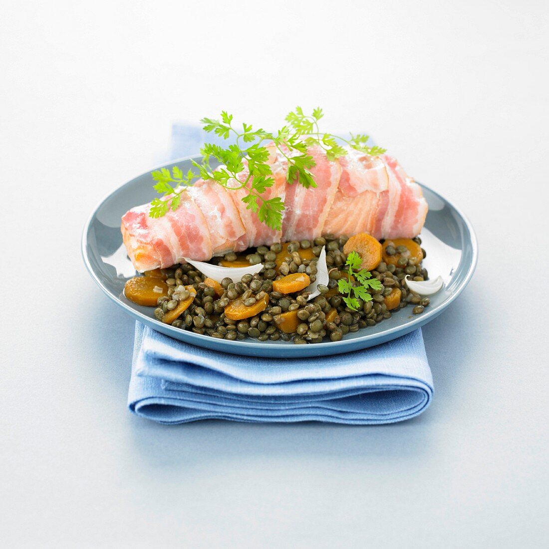 Piece of salmon wrapped in bacon, lentils with carrots