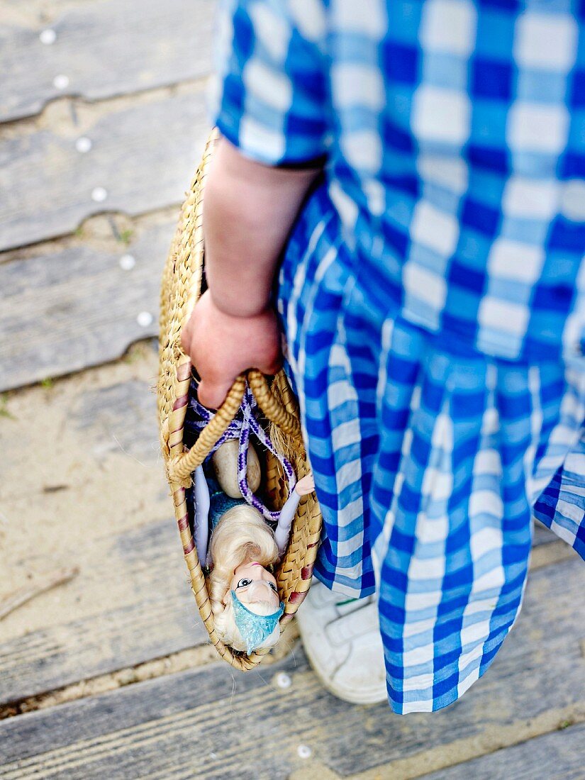 Young girl carrying a straw bag with a Barbie doll