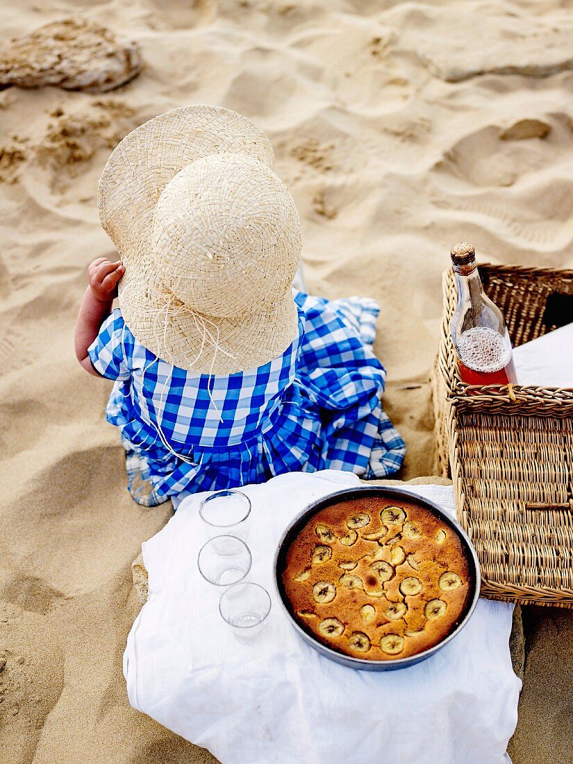 Young girl on the beach with a picnic basket and a banana cake