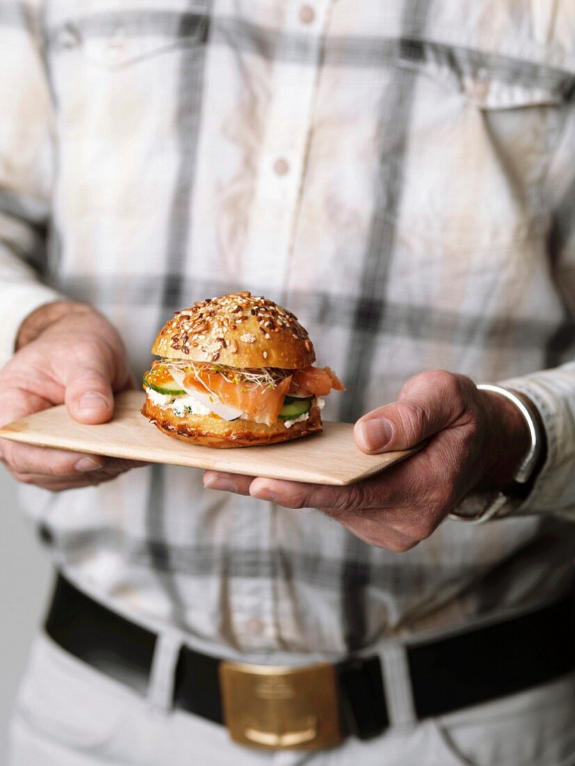 Person holding a mini salmon burger on a small wooden tray