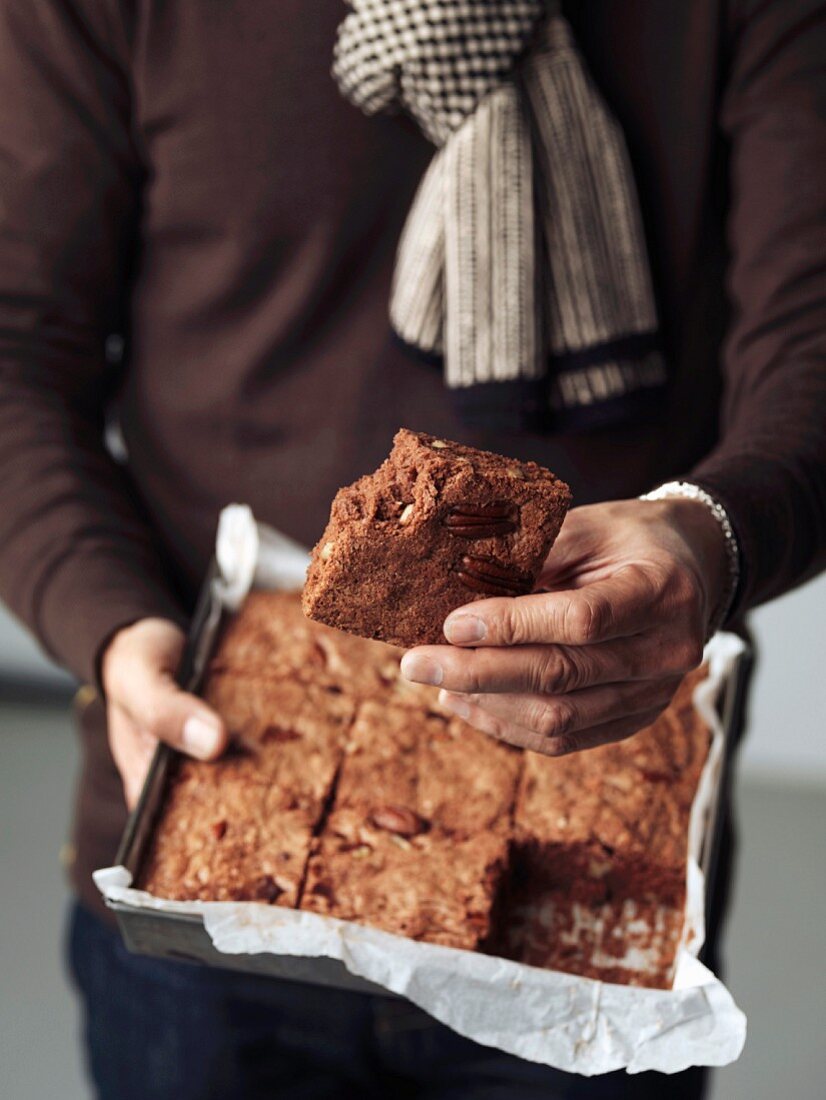 Person holding a tin mould of freshly baked brownies