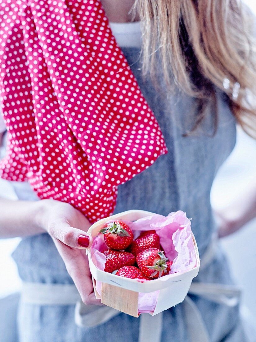 Frau hält ein Körbchen Erdbeeren