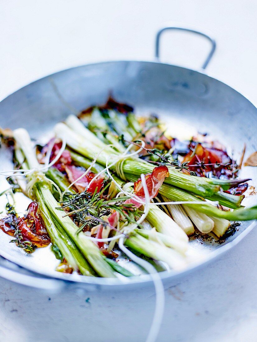 Bundles of spring onions with thyme and bacon