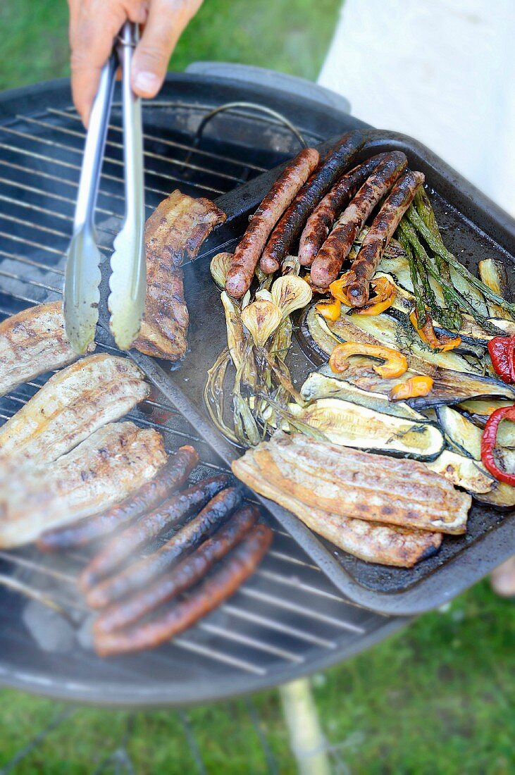 Bauchspeck, Würstchen und gegrilltes Gemüse auf einem Gartengrill