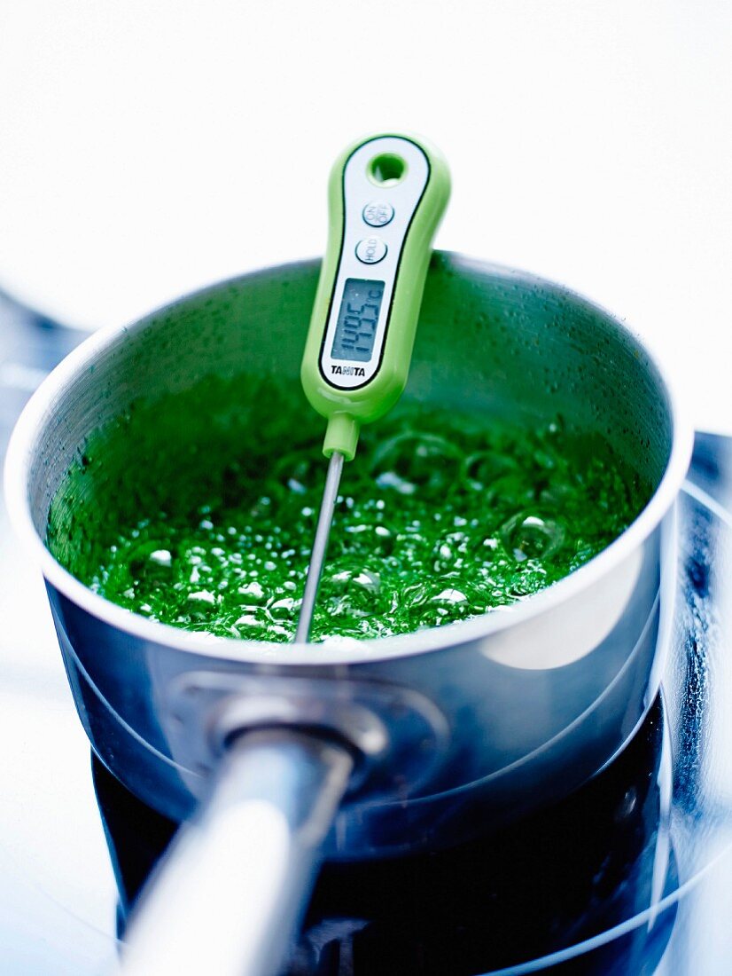 Cooking the mint syrup with the colorings while checking the temperature with a thermometer