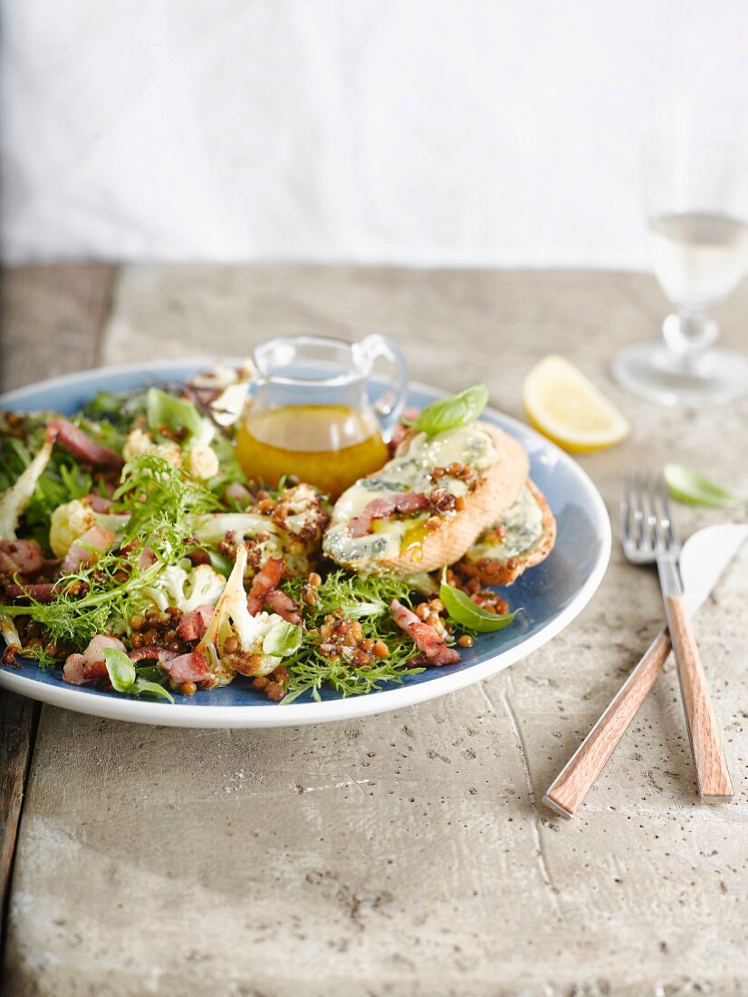 Salat mit Linsen, Friseesalat, Blumenkohl, Speckstreifen und Weißbrot mit Blauschimmelkäse