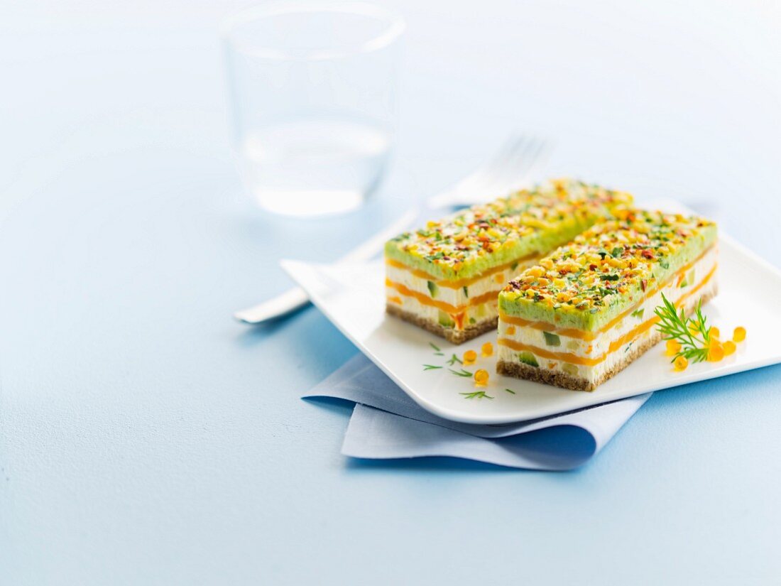 Smoked salmon, pesto, fromage frais and spring vegetable layer on white bread and decorated with almonds, red pepper and parsley