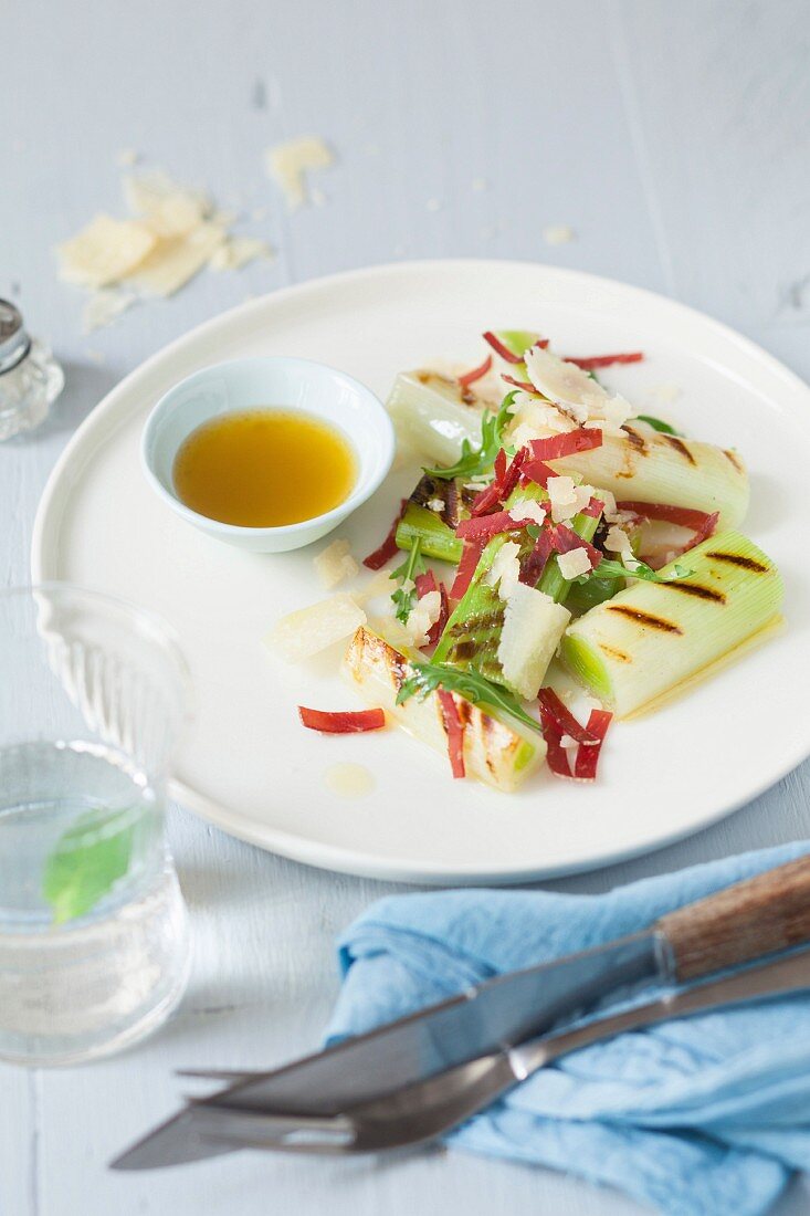 Salat mit gegrilltem Lauch, Bündnerfleisch und Parmesanspänen, daneben Schälchen mit Vinaigrette
