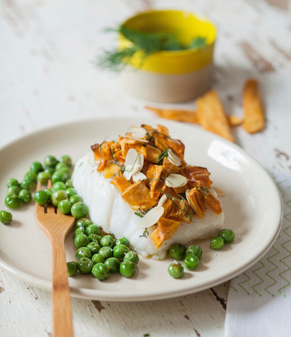 Piece of steamed cod with chanterelle and thinly sliced almond topping and fresh peas