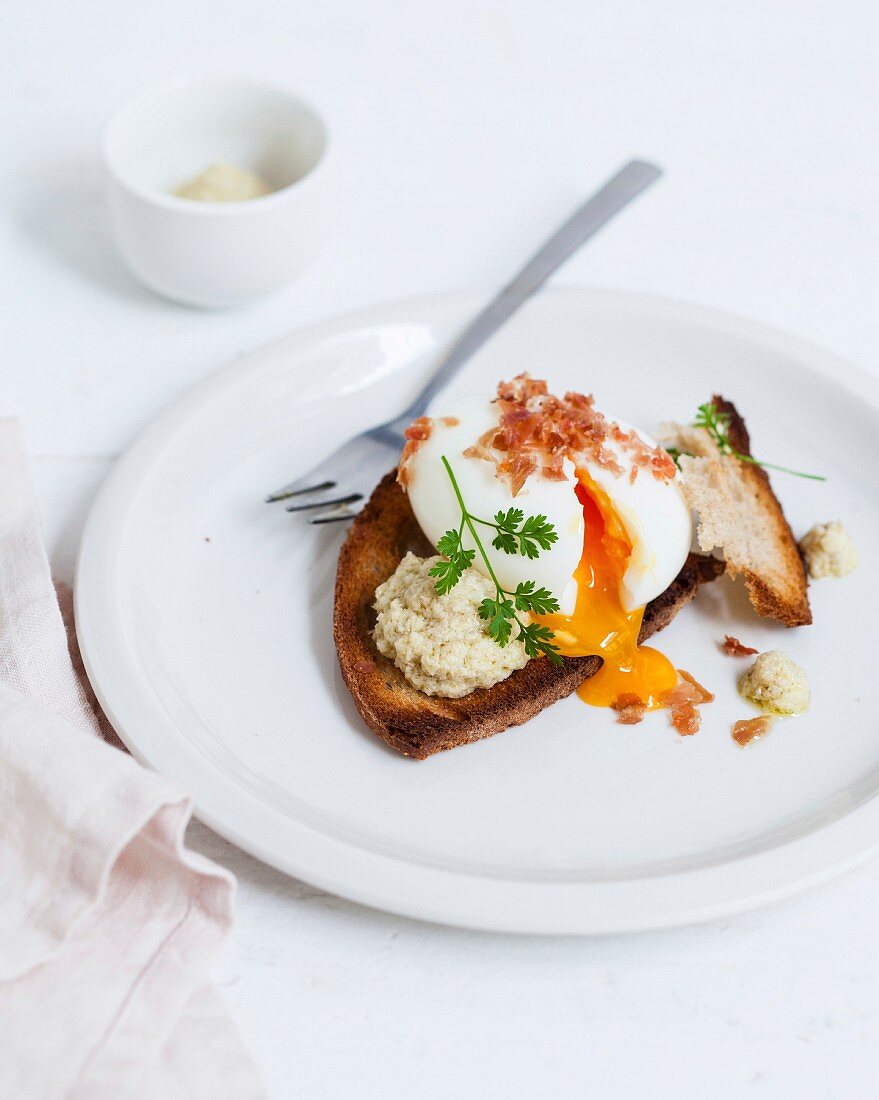 Soft-boiled egg on toast with shredded raw ham and artichoke caviar