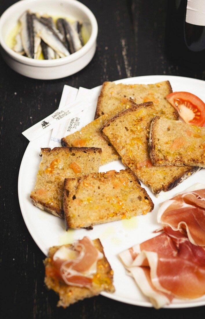 Röstbrot, eingerieben mit Knoblauch und Tomaten mit Olivenöl, Rohschinken und Sardellen