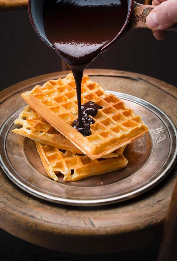 Pouring chocolate sauce onto a pile of Brussels waffles