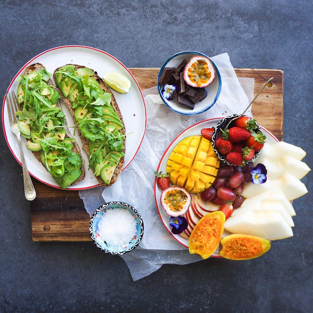 Belegte Brote mit Avocado und Rucola, Teller mit frischem Obst