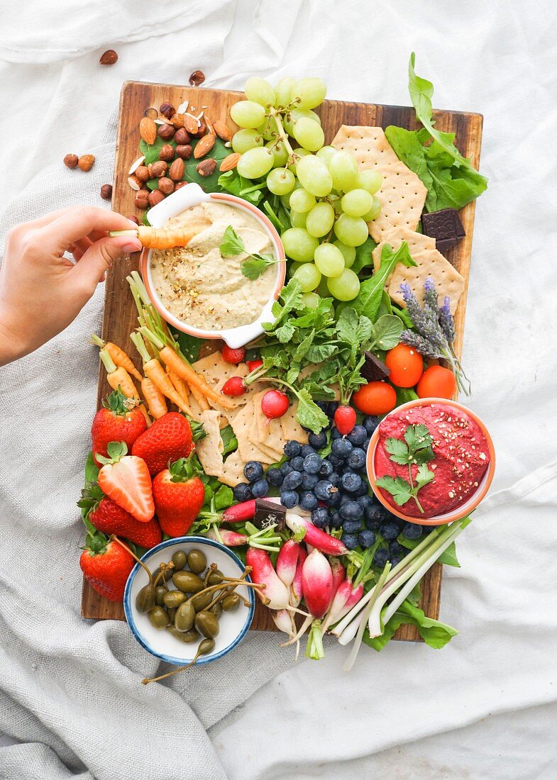 Red hummus and white hummus with a tray of crackers, fruit and raw vegetables to dip
