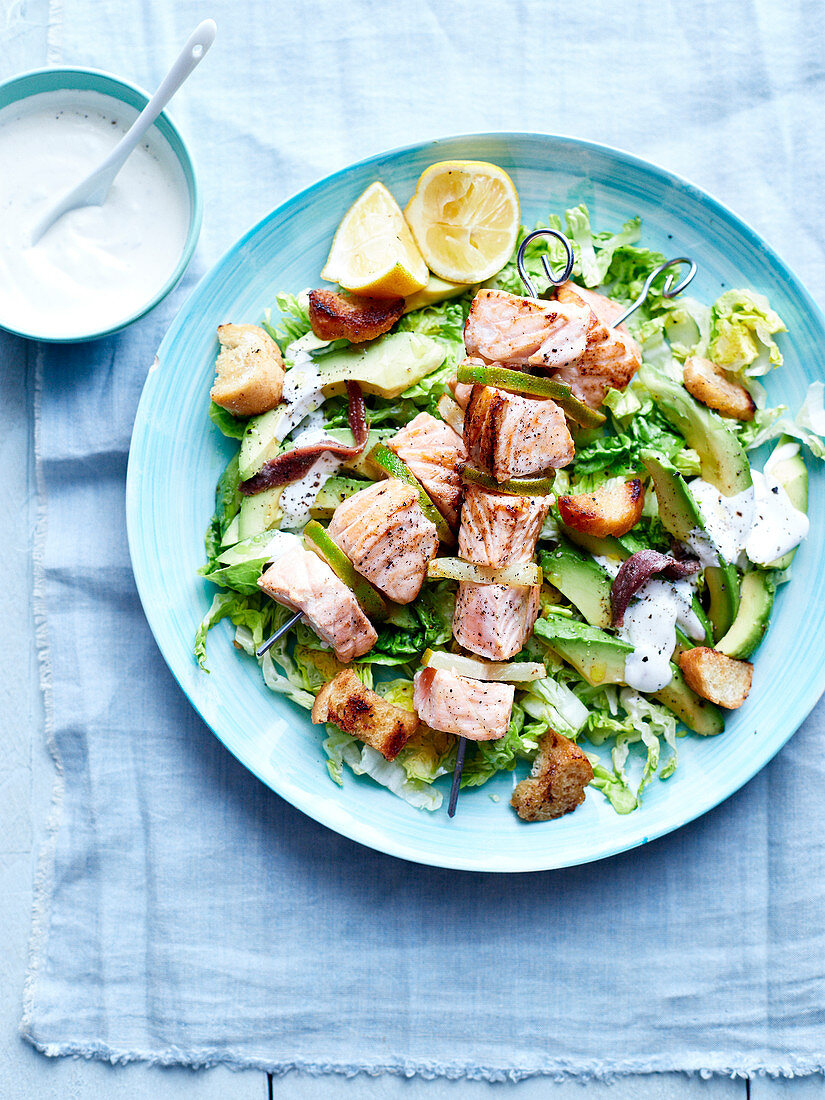 Salmon and lime brochettes with sucrine lettuce, avocado, anchovies and croutons, yoghurt sauce