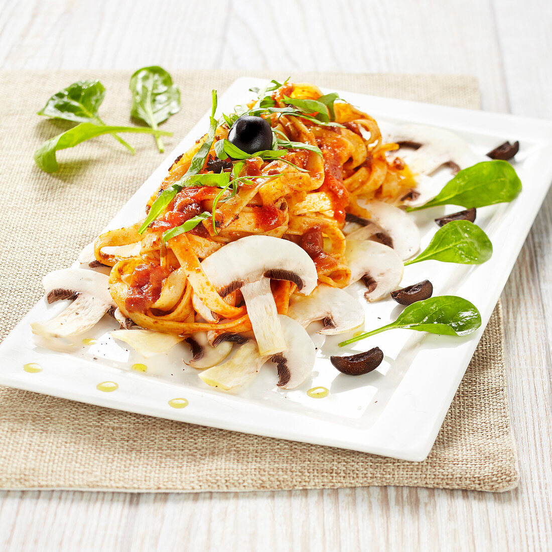 Tagliatelles in tomato sauce with mushrooms, olives and baby spinach