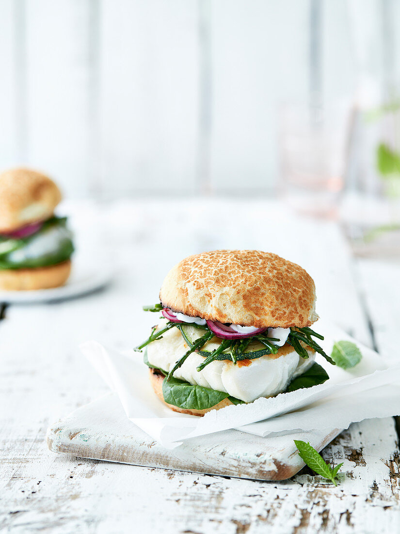 Burger mit Kabeljau, Spinat, Queller, Zucchini, roten Zwiebeln und Creme Fraiche