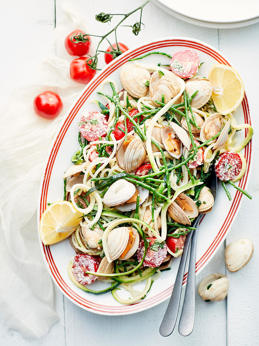 Spaghetti with clams, salicornia, zucchini strips, tomatoes and lemon