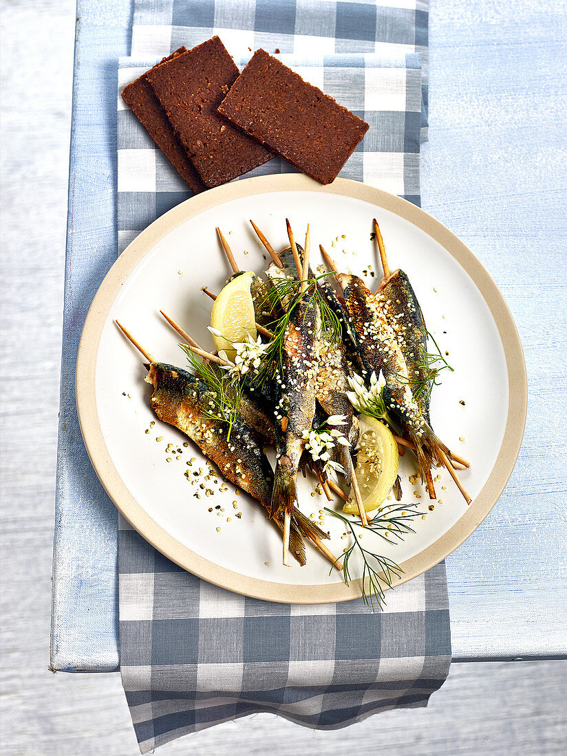 Grilled sardine skewers with lemon, dill, wild garlic flowers and hemp seeds, whole grain rye bread