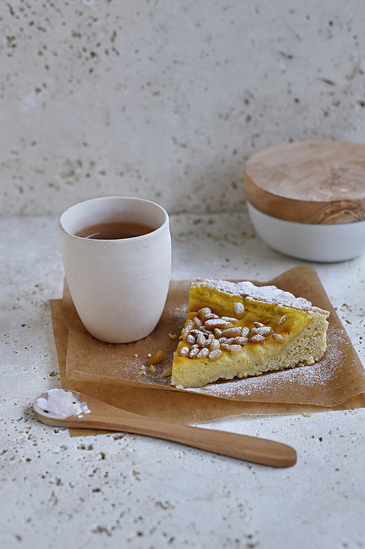 Ein Stück Zaubertorte mit gerösteten Pinienkernen und Tasse Tee