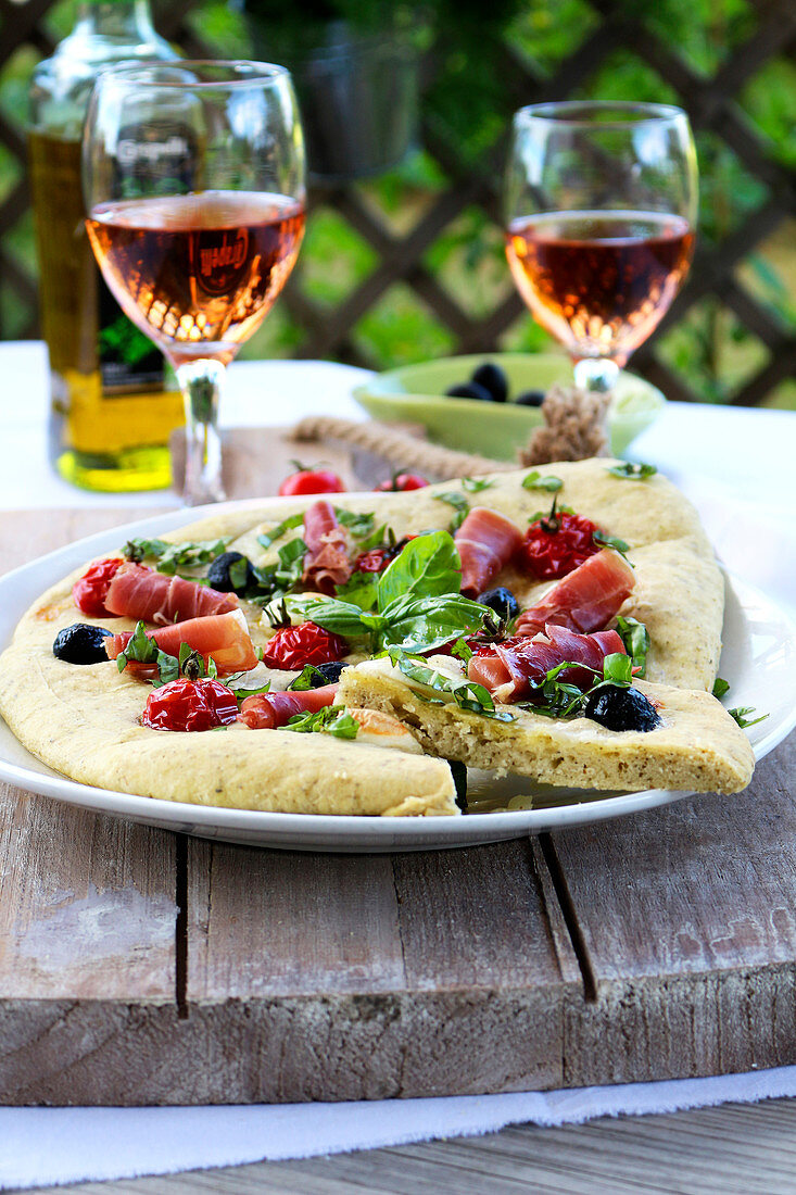 Focaccia mit Schinken, Oliven und Tomaten auf Tisch im Freien