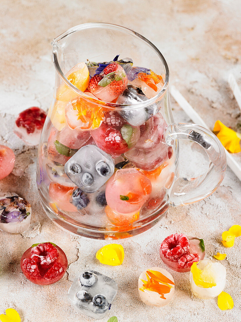 Eiswürfel mit Früchten, Kräutern und Essblüten in einer Glaskaraffe