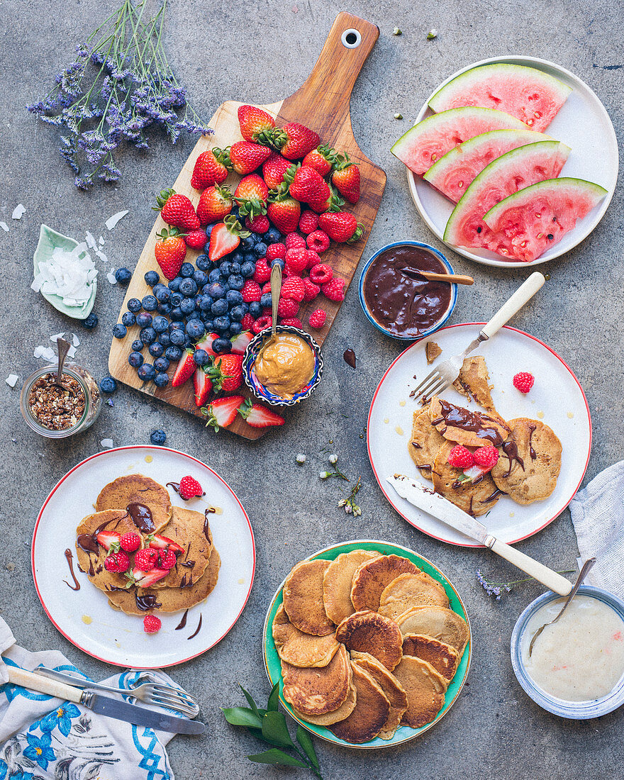 Pancakes, Holzbrett mit frischen Beeren, Schokoladensauce und Karamellsauce