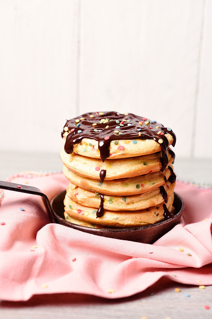 Pile of Scottish pancakes with colored sugar bits coated with dark chocolate sauce