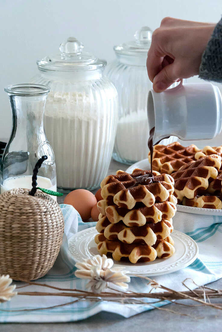 Hand pouring melted chocolate on a pile of Liège waffles