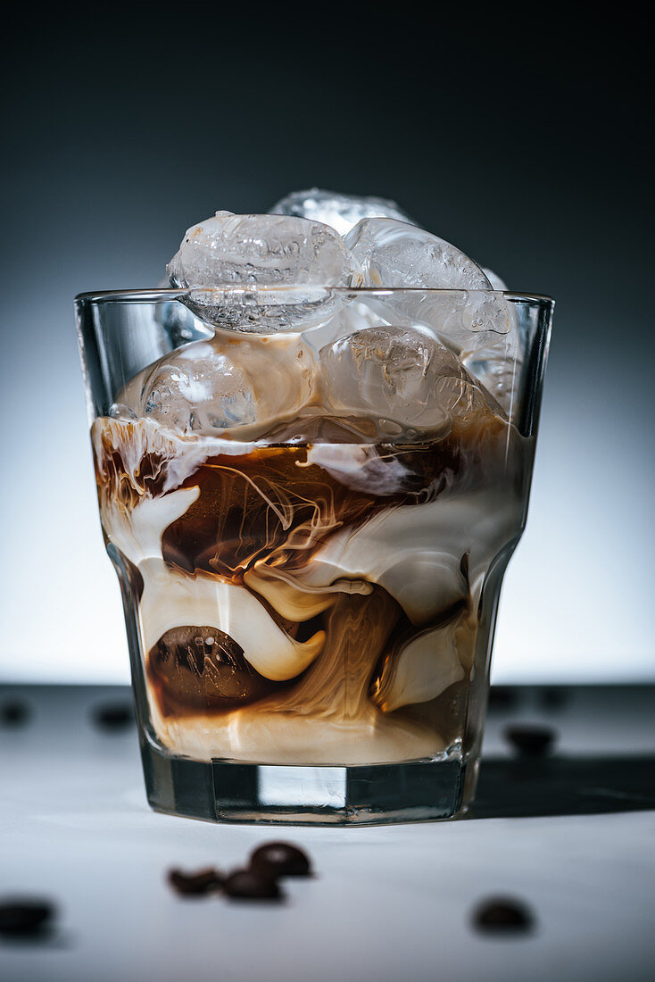 Cold brewed coffee with ice cubes and roasted coffee beans on tabletop in glass on dark backdrop