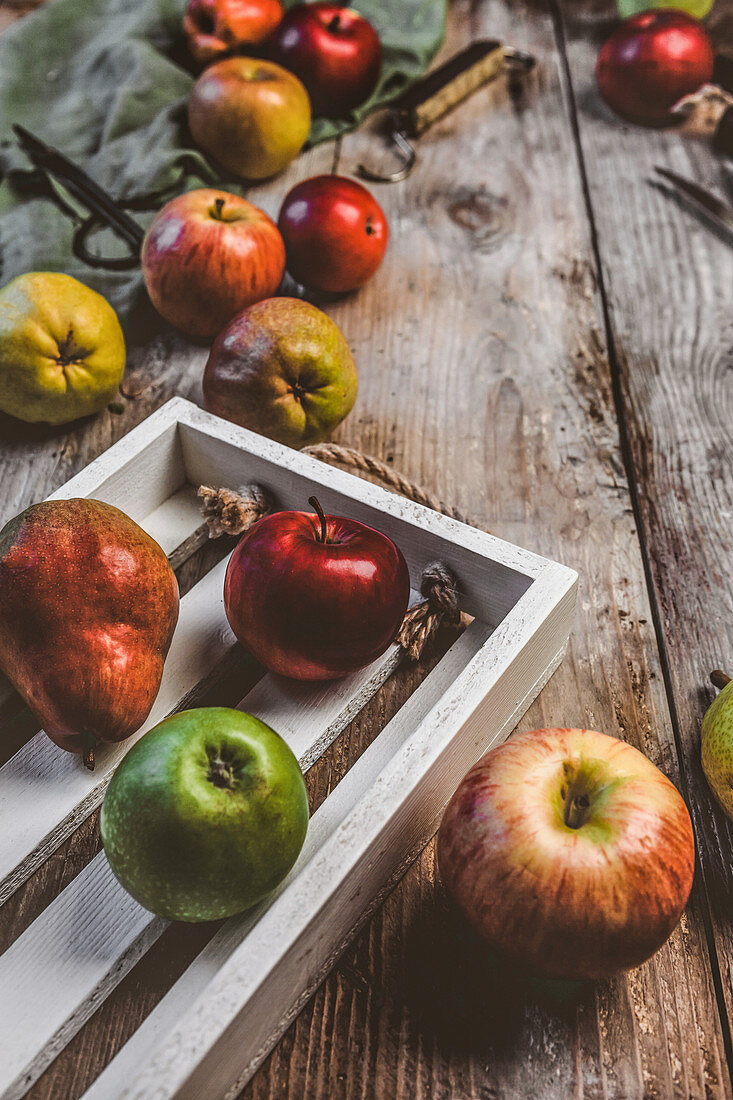 Pears, apples, wooden box, scissors, hand scales and kitchen towel on rustic tabletop