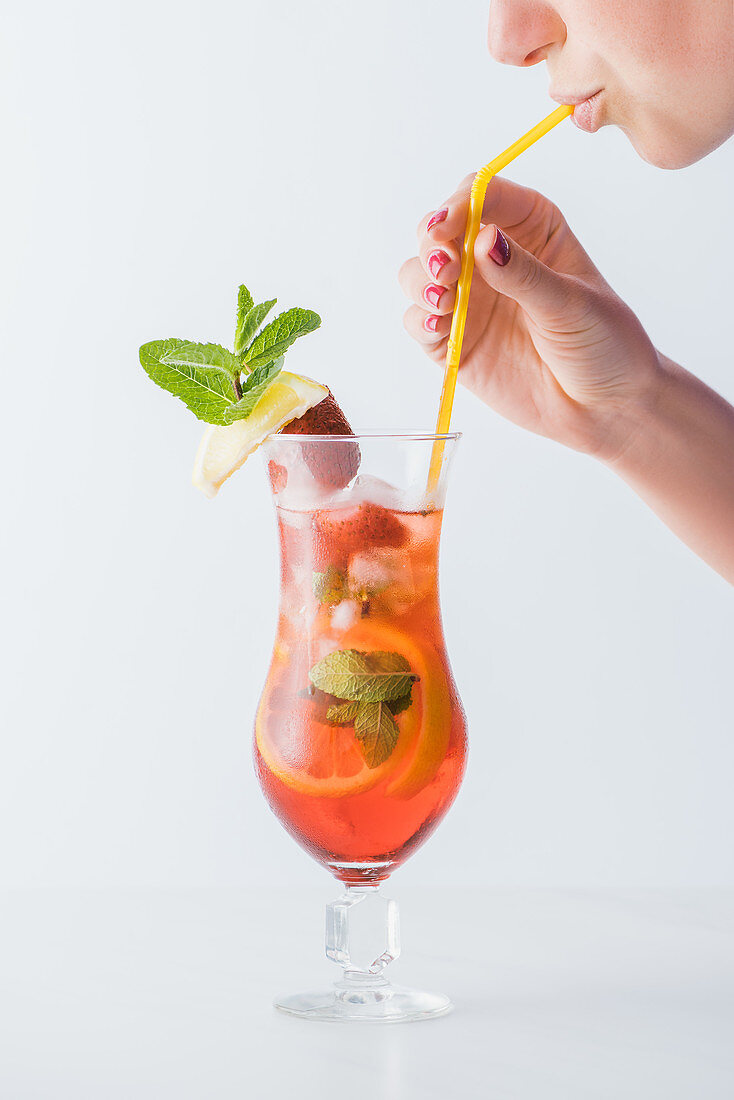 Frau trinkt Cocktail mit Zitrusfrüchten, Erdbeeren und Minze