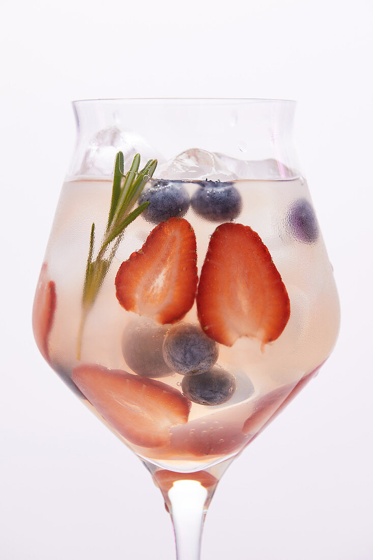 glass of lemonade with rosemary, blueberries and strawberries isolated