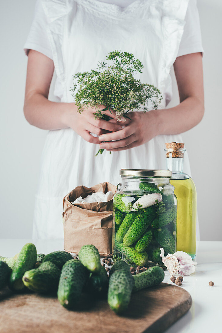 Woman preparing preserved cucumbers and holding dill at kitchen