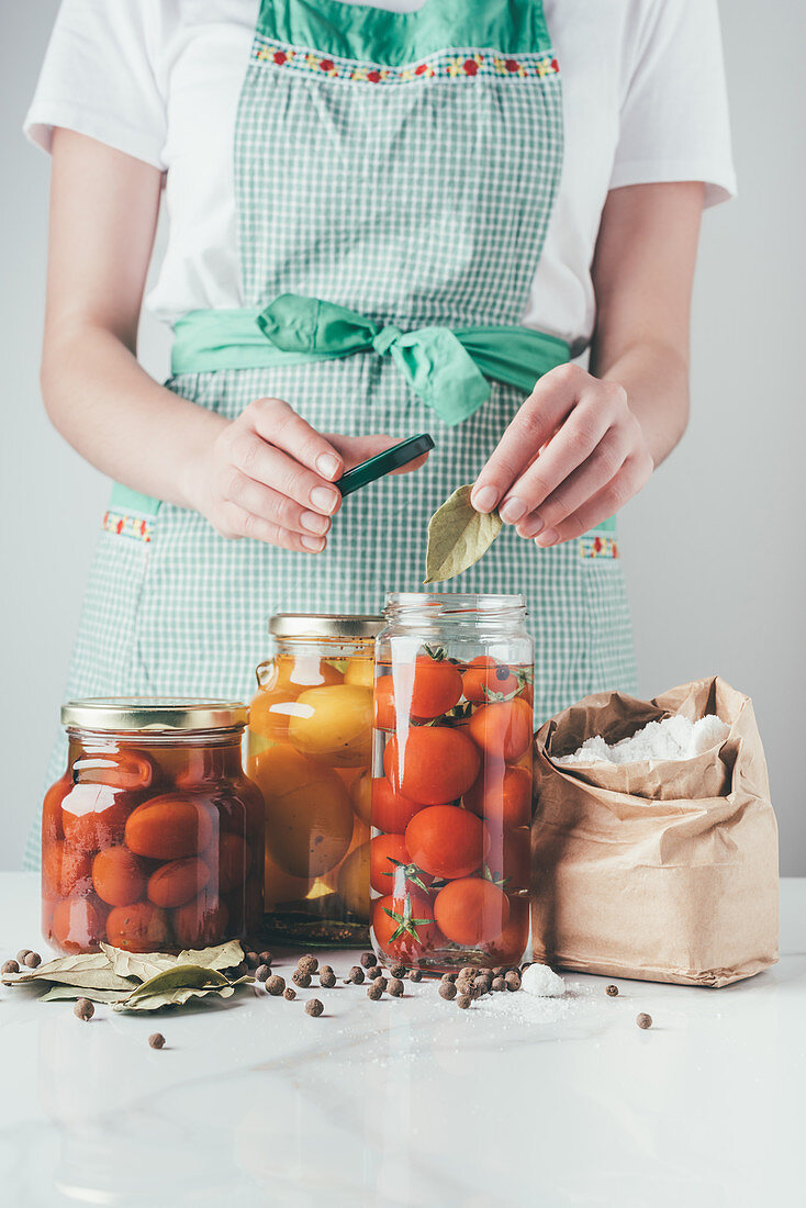 cropped image of woman adding bay leaf to preserving tomatoes at kitchen
