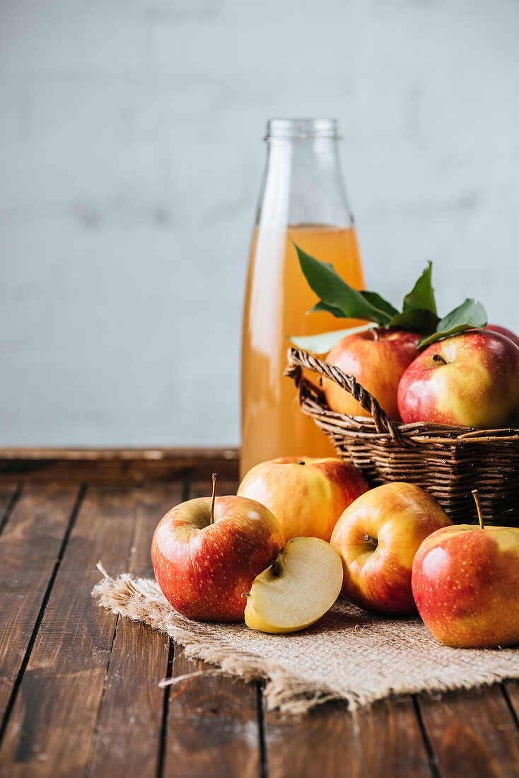 Glass bottle of apple juice and apples in basket on wooden tabletop