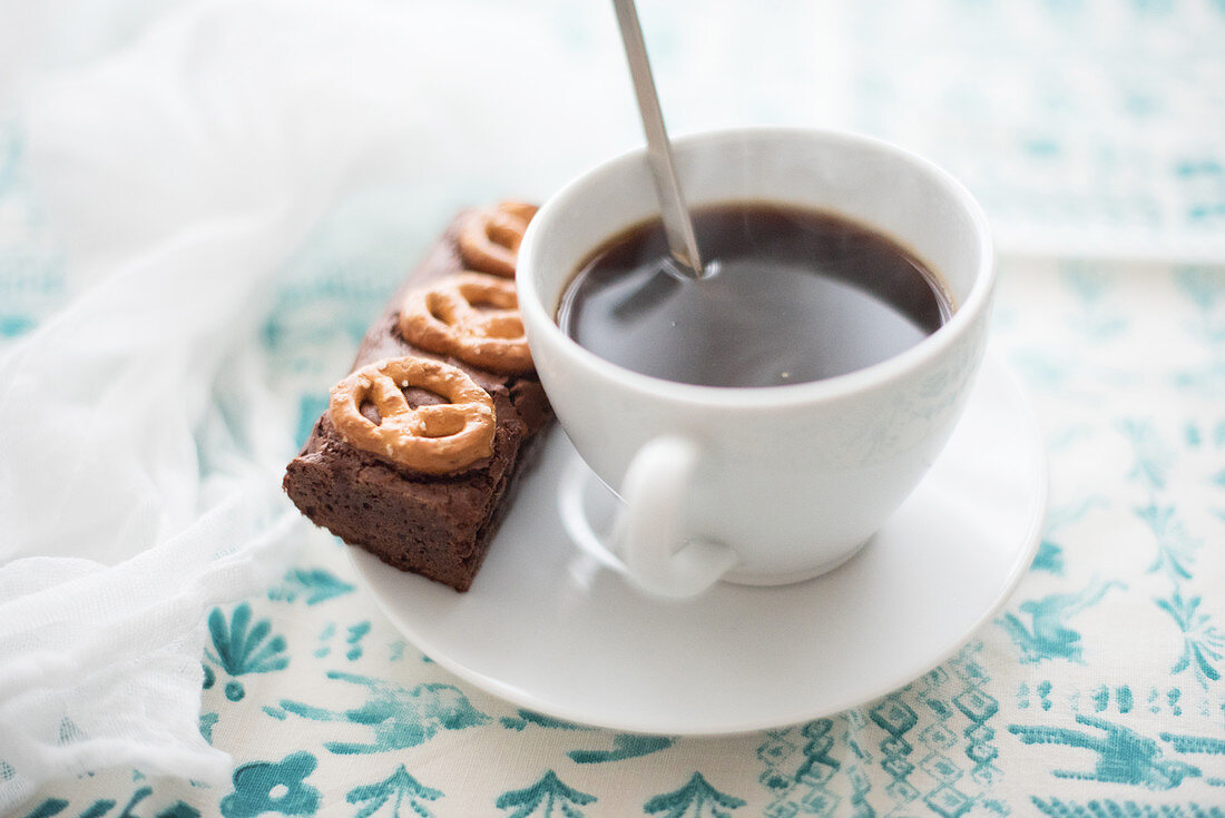 A cup of coffee with a brownie and salted pretzels