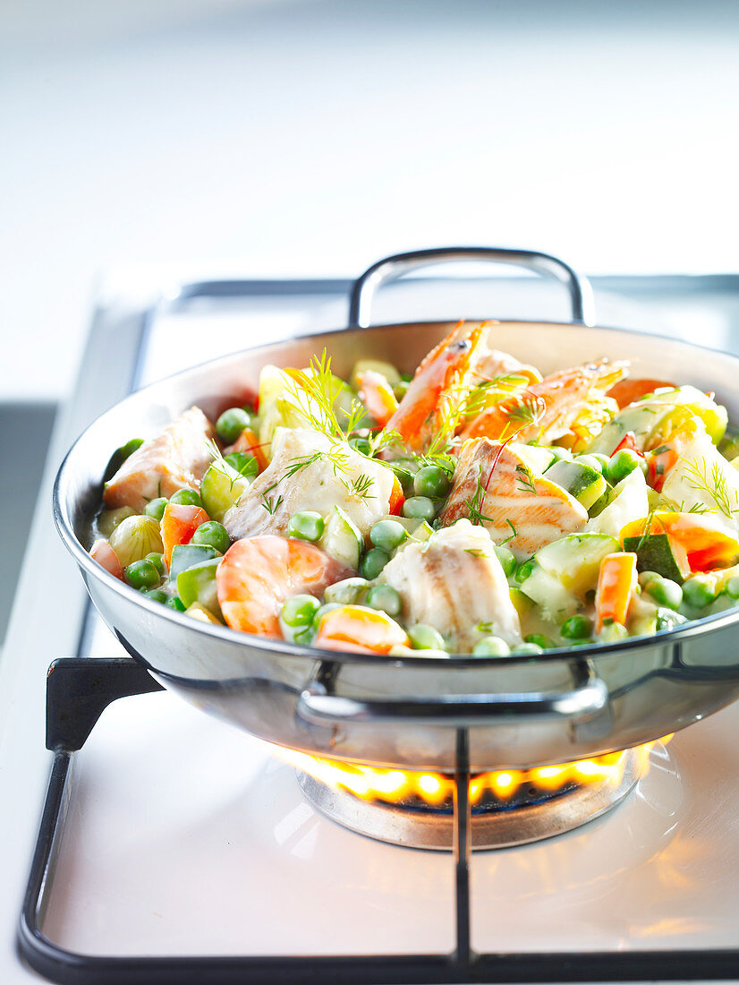 Blanquette with fish and spring vegetables on a gas stove