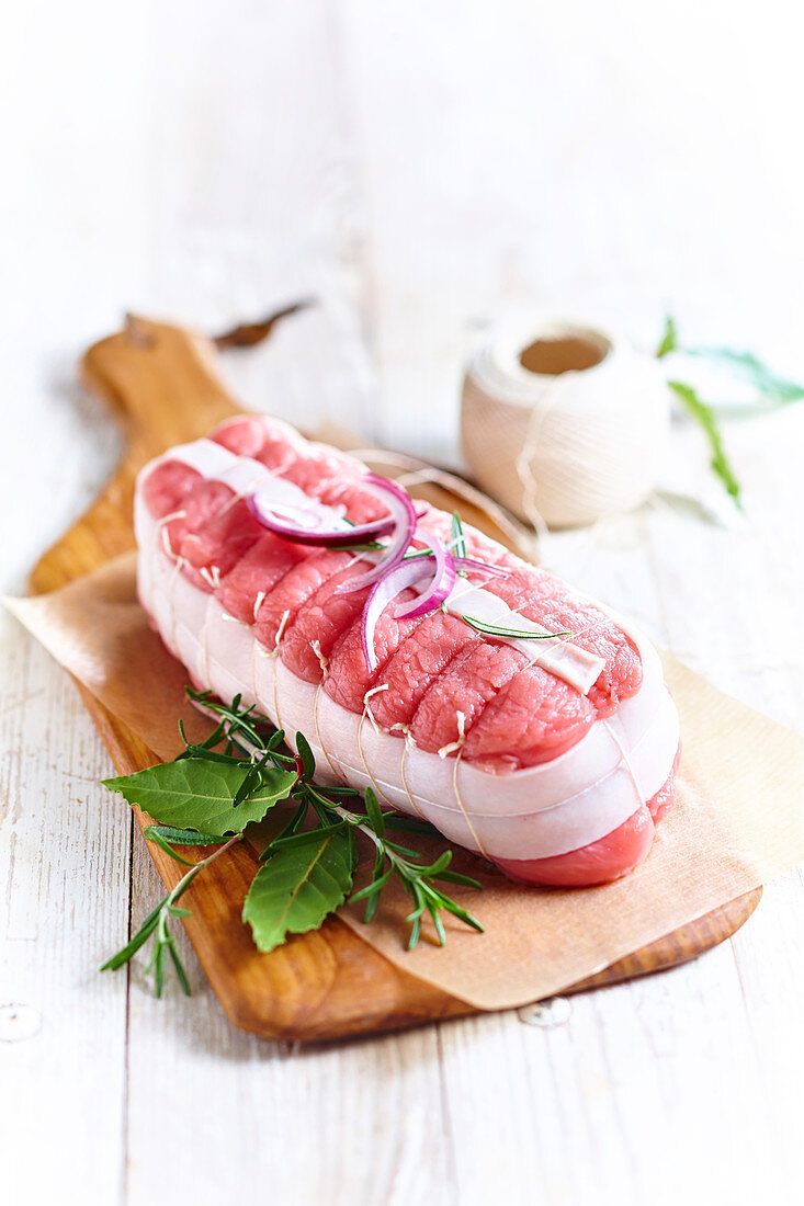 Raw roast veal with herbs on a wooden board