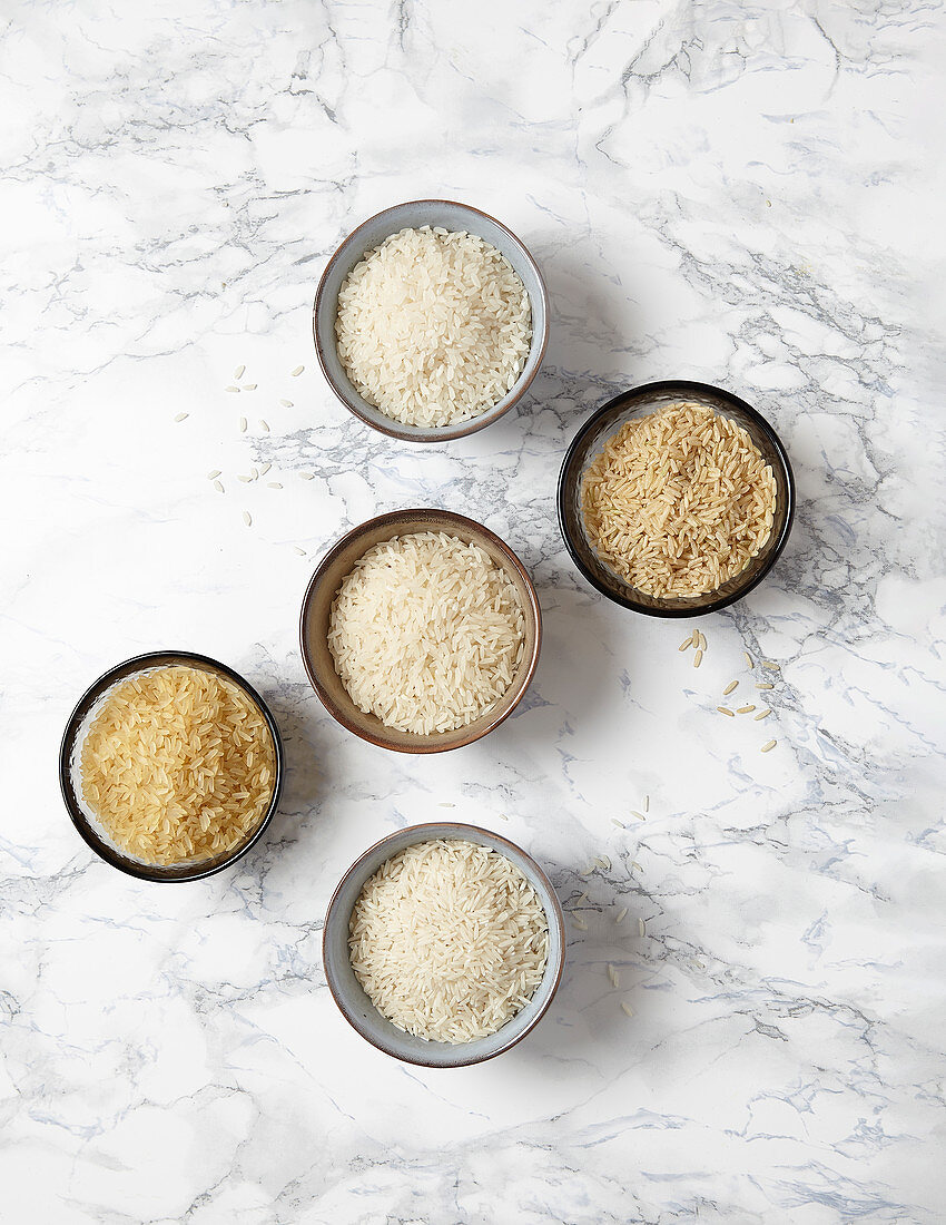 Various kinds of rice in small bowls on a marble background