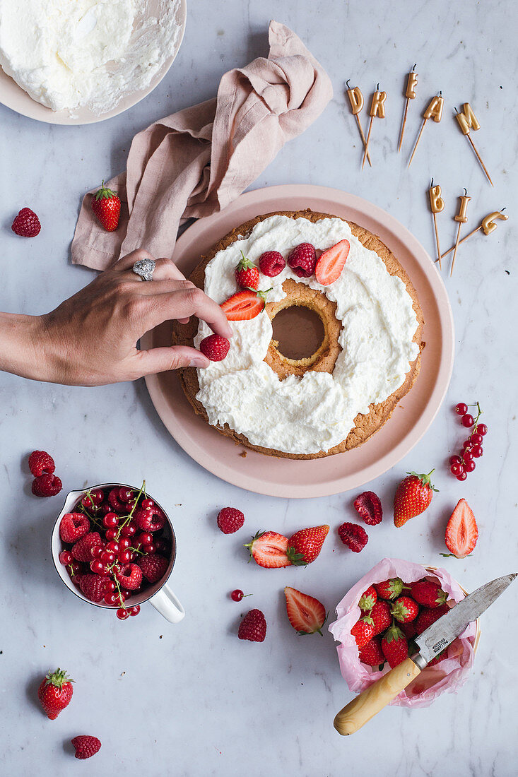 Decorating a bundt birthday cake with cream frosting and fresh red berries